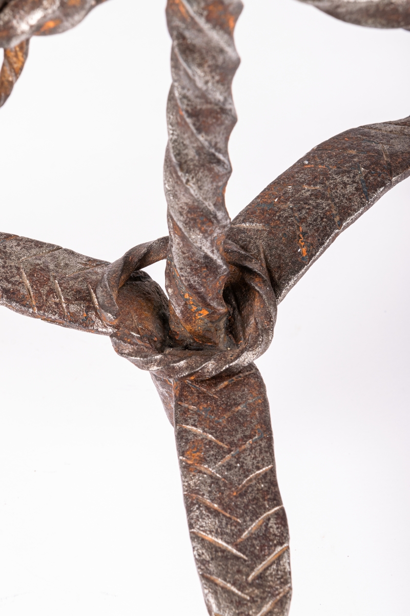 Tvåarmad ljusstake av järn. 3 fötter. Snodda tenar. I mitten en ten sluttande i en rund platta

Lappkort. Tre bågböjda fötter, två ljusarmar med smidda holkar. I mitten trebladig uppståndare, med två små hål där det troligen hängt löv eller liknande prydnad. Järntenarna spiralvridna.