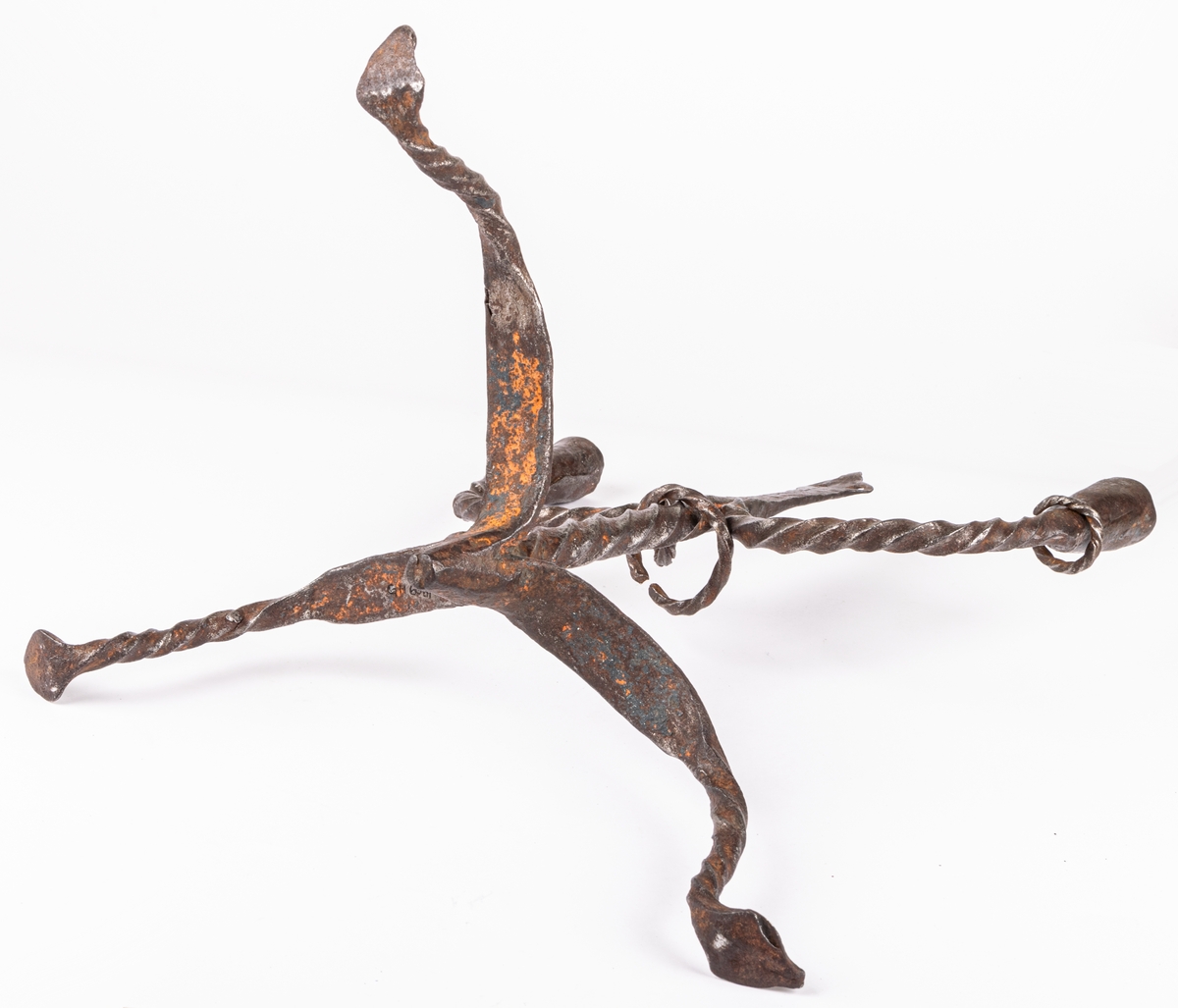 Tvåarmad ljusstake av järn. 3 fötter. Snodda tenar. I mitten en ten sluttande i en rund platta

Lappkort. Tre bågböjda fötter, två ljusarmar med smidda holkar. I mitten trebladig uppståndare, med två små hål där det troligen hängt löv eller liknande prydnad. Järntenarna spiralvridna.