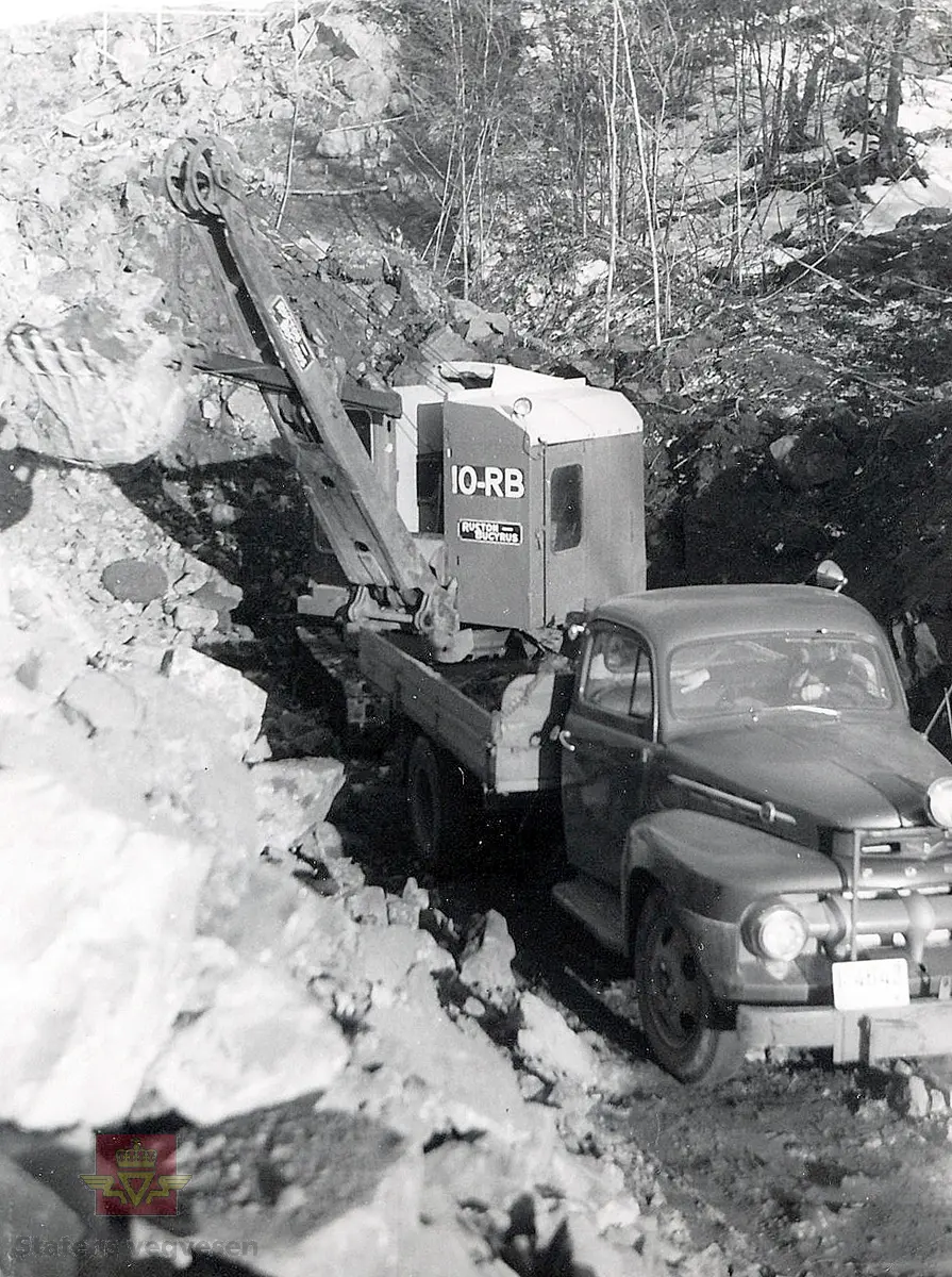 Bygging av Tromøybrua - tømming av vegskjæring.
Bilde av en Ford lastebil med kjennemerke I-4642, og en 10-RB Ruston-Bucyrus beltegravemaskin på arbeid i en vegskjæring.
Stedsnavn: Ekevalen/Krøgenes

Jf. bilder NVM 09-F-00331-00364 og NVM 09-F-00722-00744.