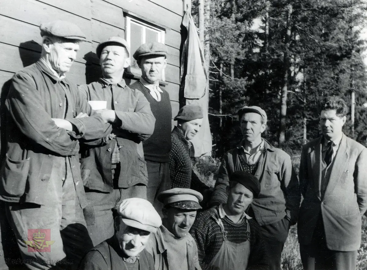 Bygging av Tromøybrua. Arbeidsgjeng fra bygging av tilførselsvegene til Tromøybrua, utenfor arbeidsbrakka.
Fra høyre: oppsynsmann Olav Nygård, Tallak Larsen. De andre er ukjente. 
Stedsnavn: Ekevalen/Krøgenes

Jf. bilder NVM 09-F-00331-00364 og NVM 09-F-00722-00744.