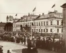 Kung Oscar II på besök i Växjö, 4 september 1900. 
Folk står och väntar på kungen i korsningen Kungsgatan/Storgatan med stadshuset/stadshotellet till höger och dåv. domkyrkans torn i bakgrunden.