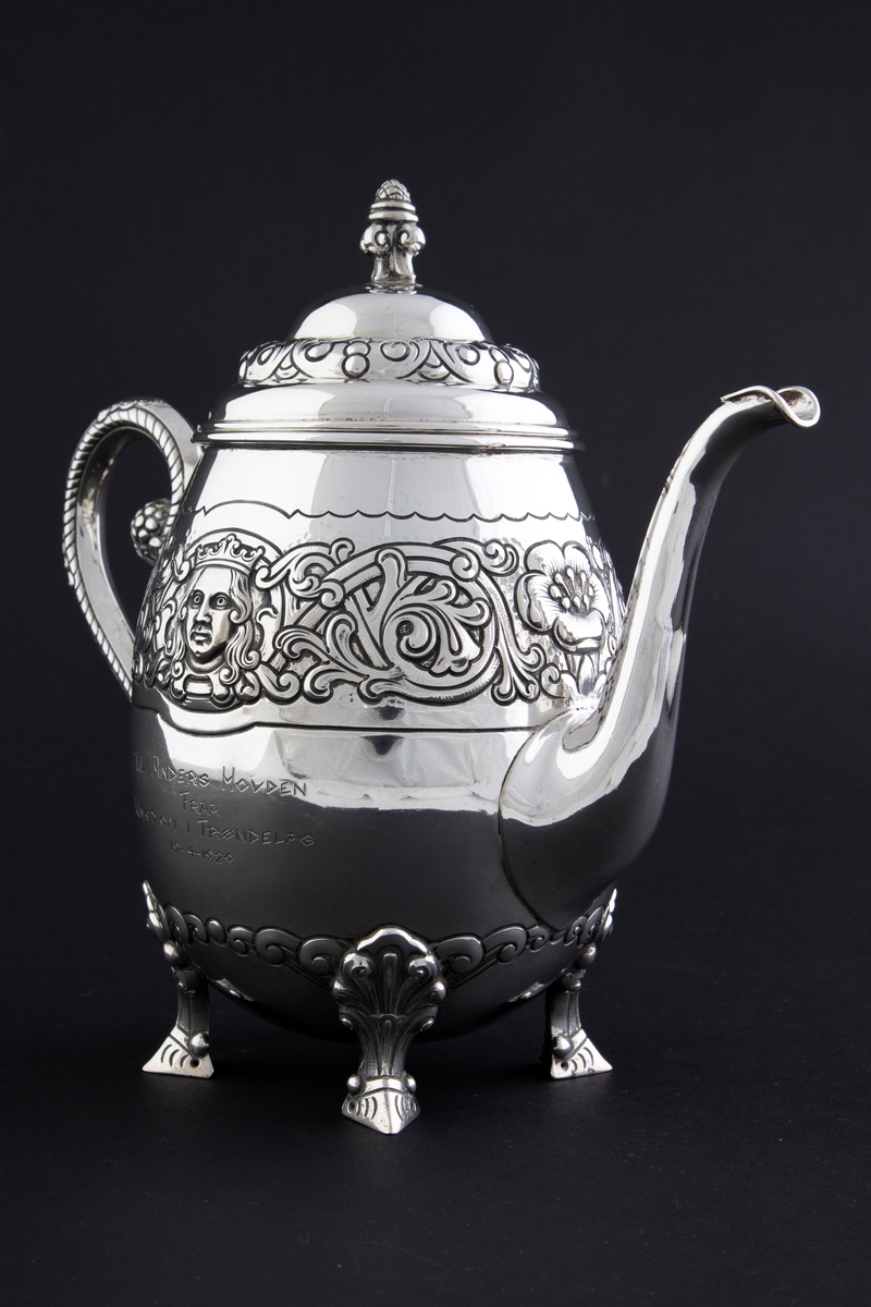 Kaffekanne med ovalformet korpus, som hviler på fire ben. Rundt midten av korpus løper en billedfrise bestående av motivscener, masker og flettverkornamentikk. Hengslet sirkulært lokk, hvor nedre del er dekorert med drevet og siselert flettverksornamentikk. Øvre del er hjelmformet med profilert lokknapp. Spiralformet hank som løper fra nedre del av korpus til skulderen. Svungen tut.