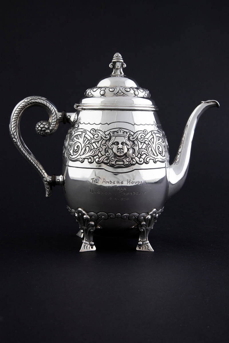 Kaffekanne med ovalformet korpus, som hviler på fire ben. Rundt midten av korpus løper en billedfrise bestående av motivscener, masker og flettverkornamentikk. Hengslet sirkulært lokk, hvor nedre del er dekorert med drevet og siselert flettverksornamentikk. Øvre del er hjelmformet med profilert lokknapp. Spiralformet hank som løper fra nedre del av korpus til skulderen. Svungen tut.