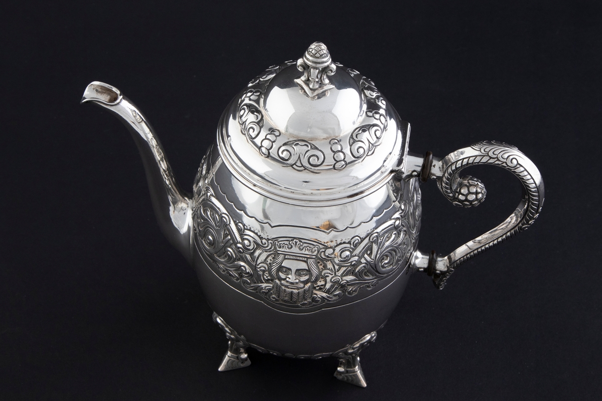 Kaffekanne med ovalformet korpus, som hviler på fire ben. Rundt midten av korpus løper en billedfrise bestående av motivscener, masker og flettverkornamentikk. Hengslet sirkulært lokk, hvor nedre del er dekorert med drevet og siselert flettverksornamentikk. Øvre del er hjelmformet med profilert lokknapp. Spiralformet hank som løper fra nedre del av korpus til skulderen. Svungen tut.