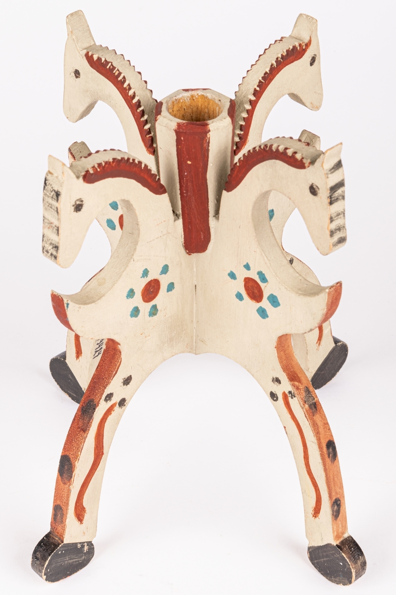 Ljusstake, trä. Ljuspipans yttre åttkantig. Fyra kontursågade ben i form av hästben som upptill avslutas i hästhuvuden. Vitmålad med dekor i rödbrunt, blått och svart. Skrift på undersidan. "April 1928 VÄRMLAND No R350"