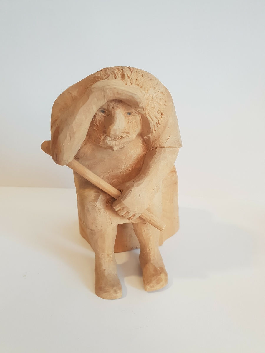Trefigur av et troll som sitter med en øks i fanget, og holder opp hånda for å skjerme for sola, eller speider. Øksen er løs. Liten lapp på baksiden med nummeret 13 på.