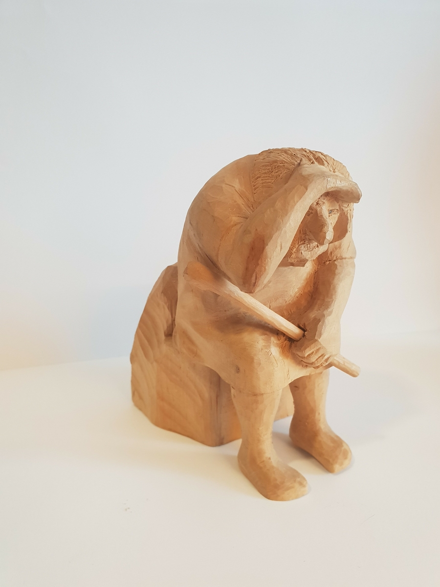Trefigur av et troll som sitter med en øks i fanget, og holder opp hånda for å skjerme for sola, eller speider. Øksen er løs. Liten lapp på baksiden med nummeret 13 på.