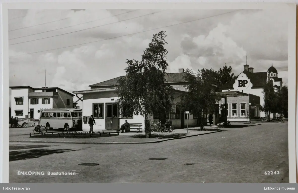 Busstationen Enköping, Gustav Adolf plan.
Gustav Adolf plan började iordningsställas 1934 och det byggdes en busstation som togs i bruk 1935. BP-macken som syns i bild flyttades till hörnet Fjärdhundragatan/Westerlundsgatan år 1961.
1967 påbörjas bygget av en ny busstation, som blir klar i juni 1967. I juli 1967 rivs den gamla busstationen och den nya tas i bruk. I den nya busstationen finns kiosk, vänthall, korvkiosk, telefonhytt och Turistinformation. Det blir den nya samlingsplatsen för stadens ungdomar.

Den nya busstationen står där i lite drygt 45år och rivs i januari 2013. Turistinformationen flyttar från Busstationen redan våren 2012, till Enköpings museum på Rådhusgatan 3.

 

Längs till vänster i bild ser vi tandläkare Hectors villa som uppfördes 1934. Villan är i funkisstil och arkitekt var Gunnar Leche.