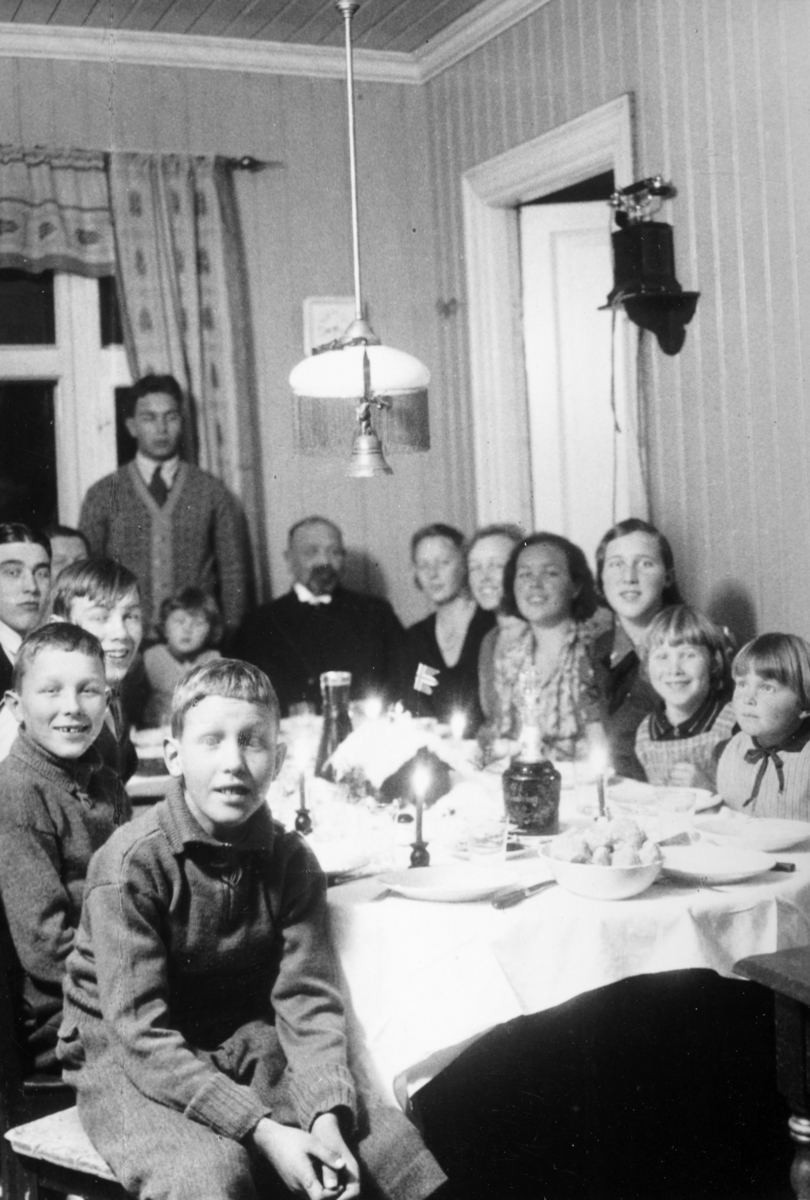 Ringsaker, Østre Alhaug, Østre Alu, julaften 1931. Familien samlet rundt middagsbord. Julemiddag. Fra venstre: Peder Alhaug (1922-), Johannes Alhaug (1920-), Eivind Alhaug (1917-), Sigurd Alhaug (1912-), Johanne Alhaug (1886-) (delvis skjult), Knut Alhaug (1929-), Johannes Alhaug (-1873-), Margit Alhaug (1904-), Karen Alhaug (1907-), Eva Alhaug (1909-), Klara Alhaug (1915-), Sidsel Alhaug (1924-), Else Alhaug (1927-). Bak står Lars Alhaug (1910-).