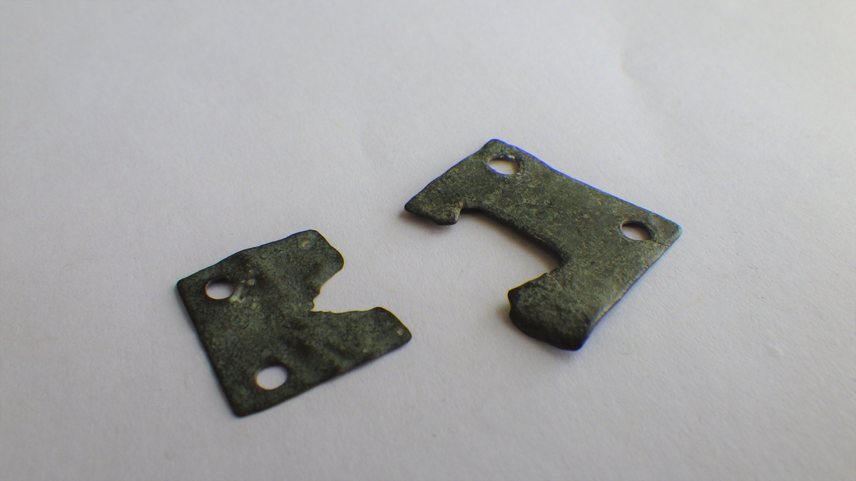 MALV: 13*15 OG 19*16, 7 MM, REKTANGULÆR BÅNDFORMET UTEN DEKOR. DET ER DEN DELENSOM FORBINDER REM MED SPENNE. 2 HULL FOR FESTE. BEGGE ER FRAGMENTARISK. REF. POST MEDIEVAL ARCH. 15 FIG. 3 (15 OG 16) S. 88. FINGERLIN FIG. 83, 84, 89 OG FLERE. 