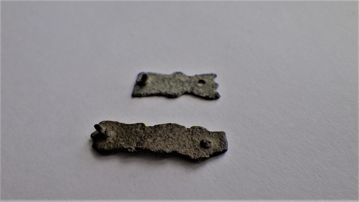 MALV: A: 12*5 B: 18*5, 5 MM, A: BÅNDFORMET MED UREGELMESSIG KANT. 2 HULL ETT MEDNAGLEFRAGMENT. B: BÅNDFORMET MED URGELMESSIG KANT. 2 HULL MED NAGLEFRAGMENT. 