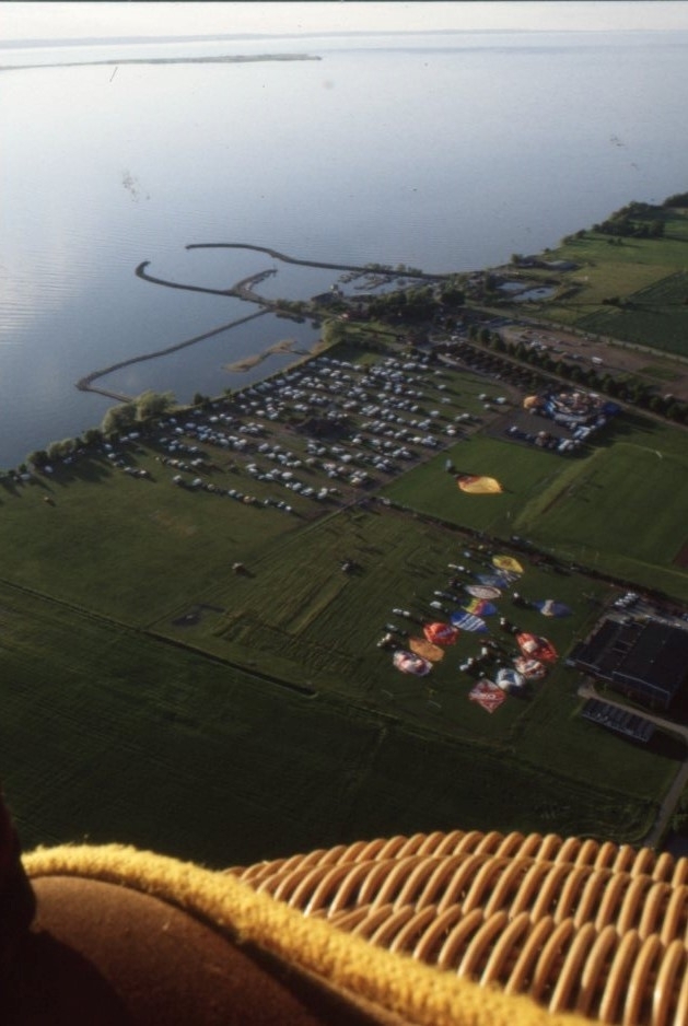 Vy över Gränna camping och Vättern. På gräsfältet bredvid campingen syns flera luftballonger utsträckta på marken. Bilden tagen från luften.