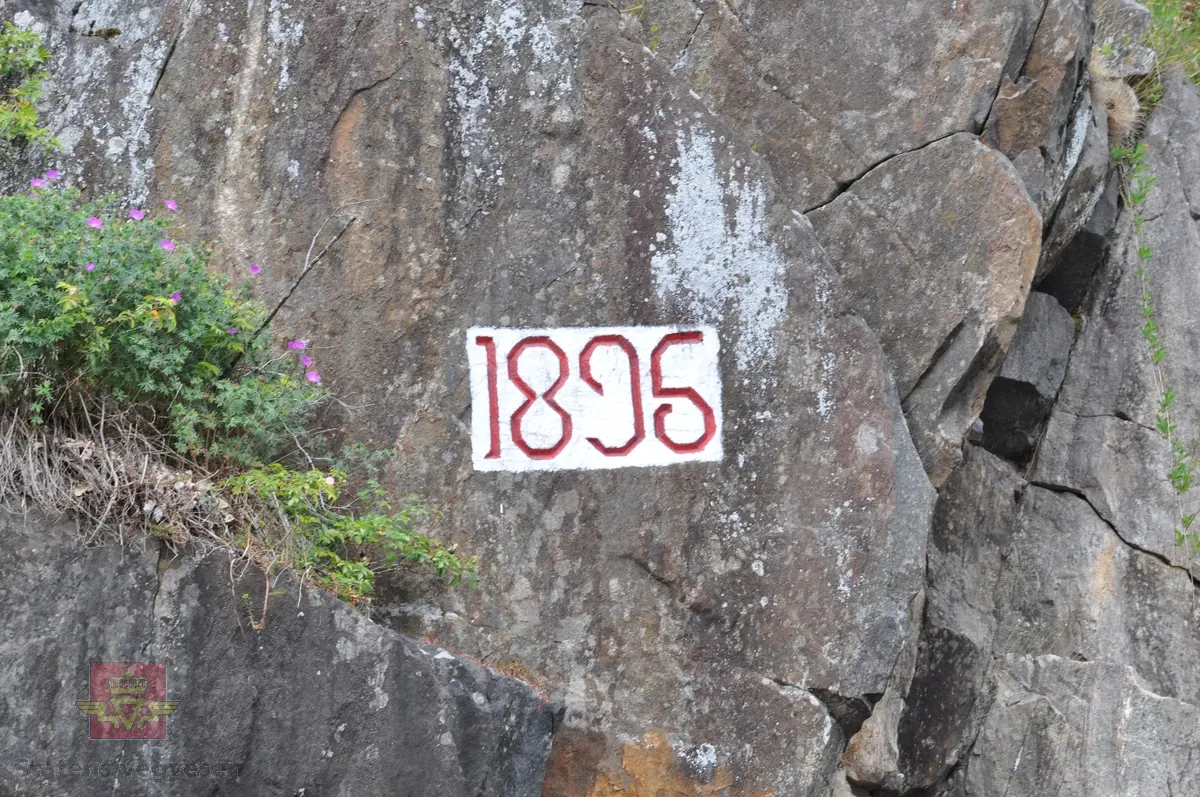 Inskripsjon i fjellvegg langs Nyvei (kommunal veg), Tvedestrand havn. Årstall i fjellveggen: 1896
Stedsnavn: Nyvei
Registrert for Statens vegvresen av Næs Jernverksmuseum i 2012 som del av prosjekt med registrering av milepæler og grensemerker mm.