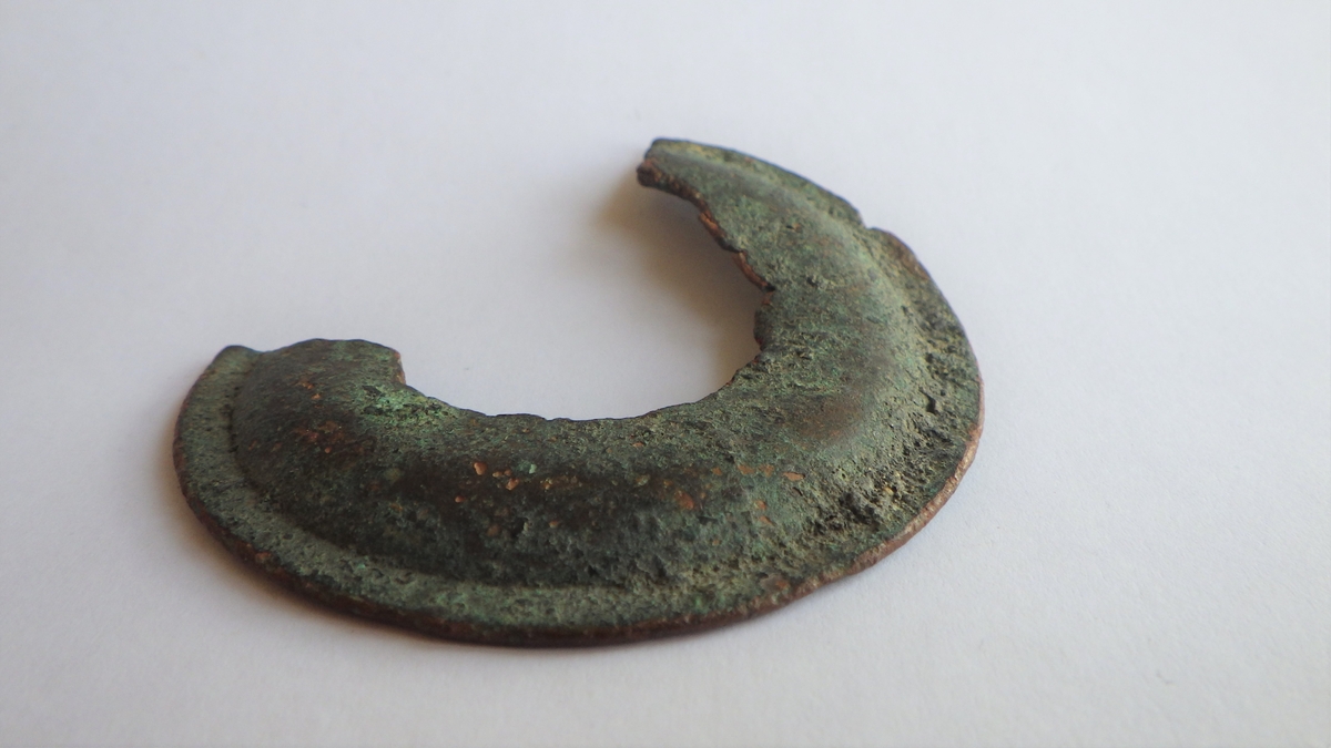 Sirkelformet metallplate med jevn ytterkant og en bruddfalte klangs hele innsiden, samt i begge kortender. det er ingen tegn til dekor, men platen er flat i ytterkant og har deretter en konveks bue som går innover. Dette er et kraftig beslag, men med ukjent bruksområde.