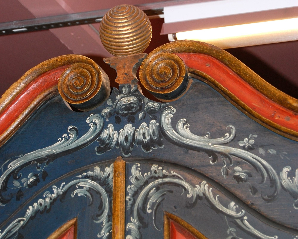 Skatoll av tre. Skapet har blå grunnfarge, og hvit og mørkeblå barokkmaling. På nederste del er det tre skuffer, med parvise håndtak laget av kobberlegering med gjennombrutt dekor. På øverste del av skapet er det to skapdører med fyllinger. I fyllingene er det malt dekor med motiv av to mennesker med blomster og fugl i hendene. Skapet har konveks koll, med to lister med gullbelagte kanter som ender i to volutter på midten. Mellom voluttene er det en gullbelagt kule med dekorative tverrsnitt. På den nedfellbare platen er det to fyllinger med profilerte lister, og malt dekor av landskapsmotiv.