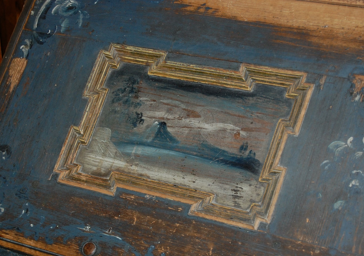 Skatoll av tre. Skapet har blå grunnfarge, og hvit og mørkeblå barokkmaling. På nederste del er det tre skuffer, med parvise håndtak laget av kobberlegering med gjennombrutt dekor. På øverste del av skapet er det to skapdører med fyllinger. I fyllingene er det malt dekor med motiv av to mennesker med blomster og fugl i hendene. Skapet har konveks koll, med to lister med gullbelagte kanter som ender i to volutter på midten. Mellom voluttene er det en gullbelagt kule med dekorative tverrsnitt. På den nedfellbare platen er det to fyllinger med profilerte lister, og malt dekor av landskapsmotiv.