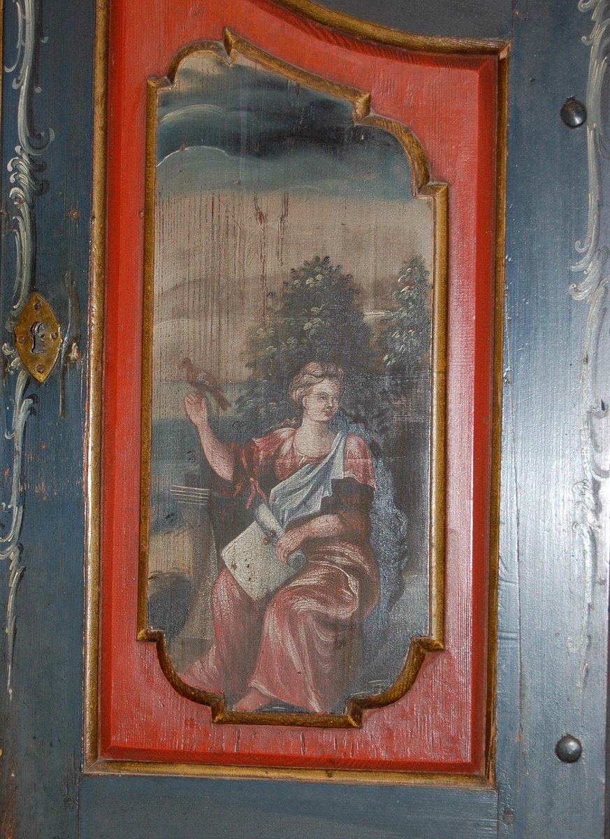 Skatoll av tre. Skapet har blå grunnfarge, og hvit og mørkeblå barokkmaling. På nederste del er det tre skuffer, med parvise håndtak laget av kobberlegering med gjennombrutt dekor. På øverste del av skapet er det to skapdører med fyllinger. I fyllingene er det malt dekor med motiv av to mennesker med blomster og fugl i hendene. Skapet har konveks koll, med to lister med gullbelagte kanter som ender i to volutter på midten. Mellom voluttene er det en gullbelagt kule med dekorative tverrsnitt. På den nedfellbare platen er det to fyllinger med profilerte lister, og malt dekor av landskapsmotiv.