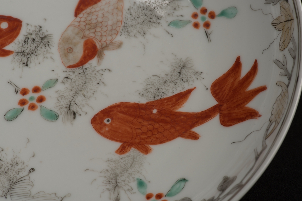 Runt fat av vitt porslin. 
Bemålad med mångfärgad, polykrom, dekor i form av fyra karpfiskar, blommor och blad. Fatet har en låg skålform utan bräm samt en oglaserad fotring. På undersidan finns en text om att tallriken tillhört det Gradmanska hemmet.