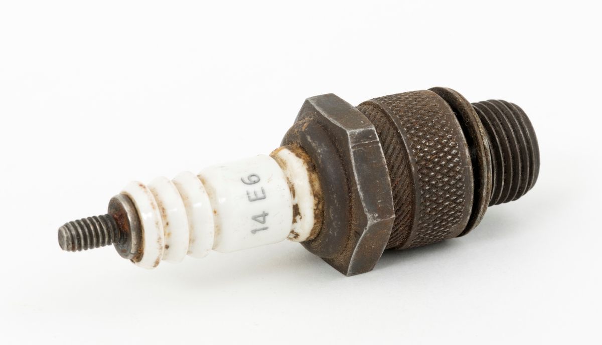Tennplugg av merket «Prestolite». Dette er et nordamerikansk selskap som ble etablert i 1911 for å produsere bilelektriske artikler. Denne pluggen er drøyt 6,8 centimeter lang. Gjengetappen som ble innskrudd øverst i motorens sylinder har en diameter på 1,4 centimeter. Pluggen veier 54 gram. Det kvite porselenselementet som isolerer den øvre delen av pluggen er merket med fabrikantnavnet «prestolite» og tall- og bokstavkoden «14 E6». Denne koden angir sannsynligvis varmeverdien til pluggen. Tennpluggens oppgave er å omdanne høyspenning fra bensinmotorens tennspole til en gnist i forbrenningskammeret øverst i sylinderen. Tennpluggen ble avlevert til museet i ei kasse som inneholdt materiell fra ei smie.