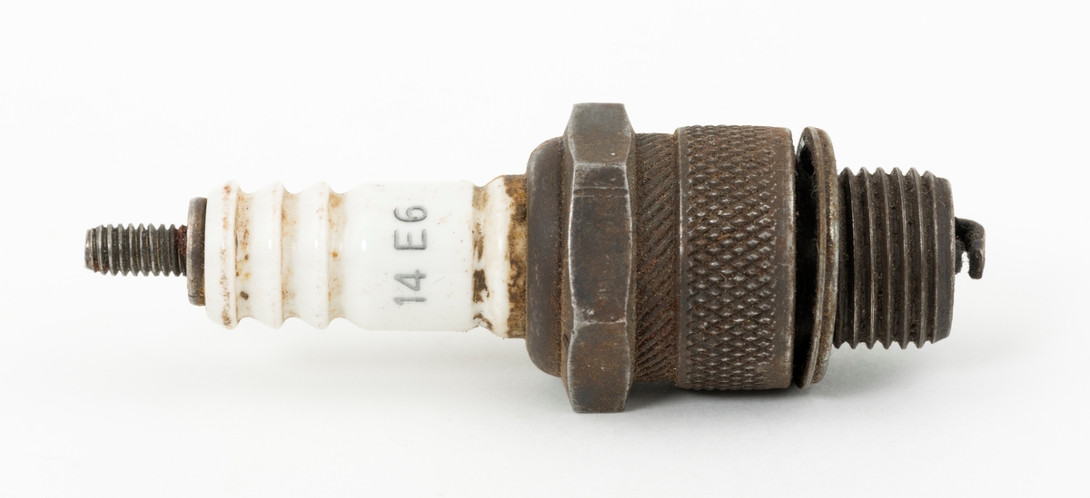 Tennplugg av merket «Prestolite». Dette er et nordamerikansk selskap som ble etablert i 1911 for å produsere bilelektriske artikler. Denne pluggen er drøyt 6,8 centimeter lang. Gjengetappen som ble innskrudd øverst i motorens sylinder har en diameter på 1,4 centimeter. Pluggen veier 54 gram. Det kvite porselenselementet som isolerer den øvre delen av pluggen er merket med fabrikantnavnet «prestolite» og tall- og bokstavkoden «14 E6». Denne koden angir sannsynligvis varmeverdien til pluggen. Tennpluggens oppgave er å omdanne høyspenning fra bensinmotorens tennspole til en gnist i forbrenningskammeret øverst i sylinderen. Tennpluggen ble avlevert til museet i ei kasse som inneholdt materiell fra ei smie.