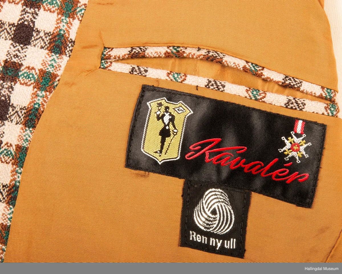 Kavaler dressjakke mønstrete ullstoff. Sennepsgult syntetisk silkefor. Jakka har skulderputer, store klaffer på lommene, 2 splitter bak.   Den er knept med 2 plastknapper midt framme.  1 pynteknapp på hvert erme.  Store slag.