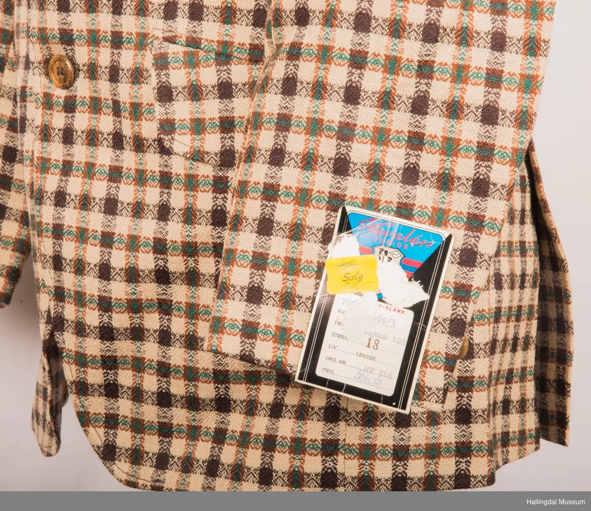 Kavaler dressjakke mønstrete ullstoff. Sennepsgult syntetisk silkefor. Jakka har skulderputer, store klaffer på lommene, 2 splitter bak.   Den er knept med 2 plastknapper midt framme.  1 pynteknapp på hvert erme.  Store slag.