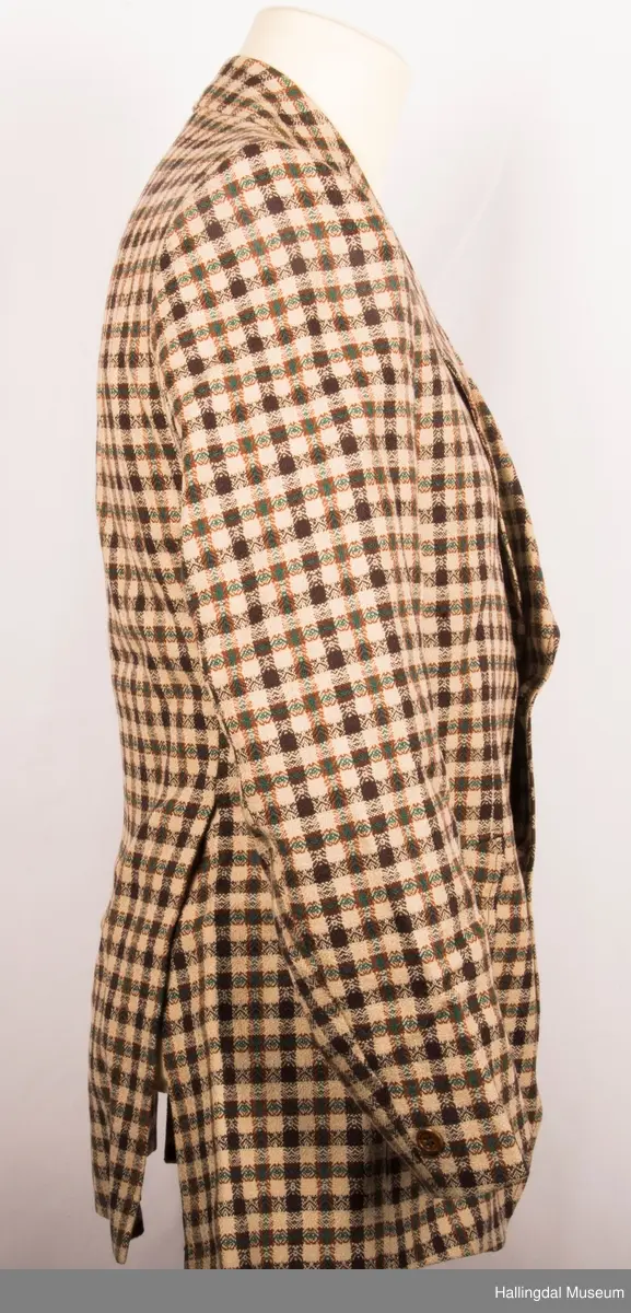 Kavaler dressjakke mønstrete ullstoff. Sennepsgult syntetisk silkefor. Jakka har skulderputer, store klaffer på lommene, 2 splitter bak.   Den er knept med 2 plastknapper midt framme.  1 pynteknapp på hvert erme.  Store slag.