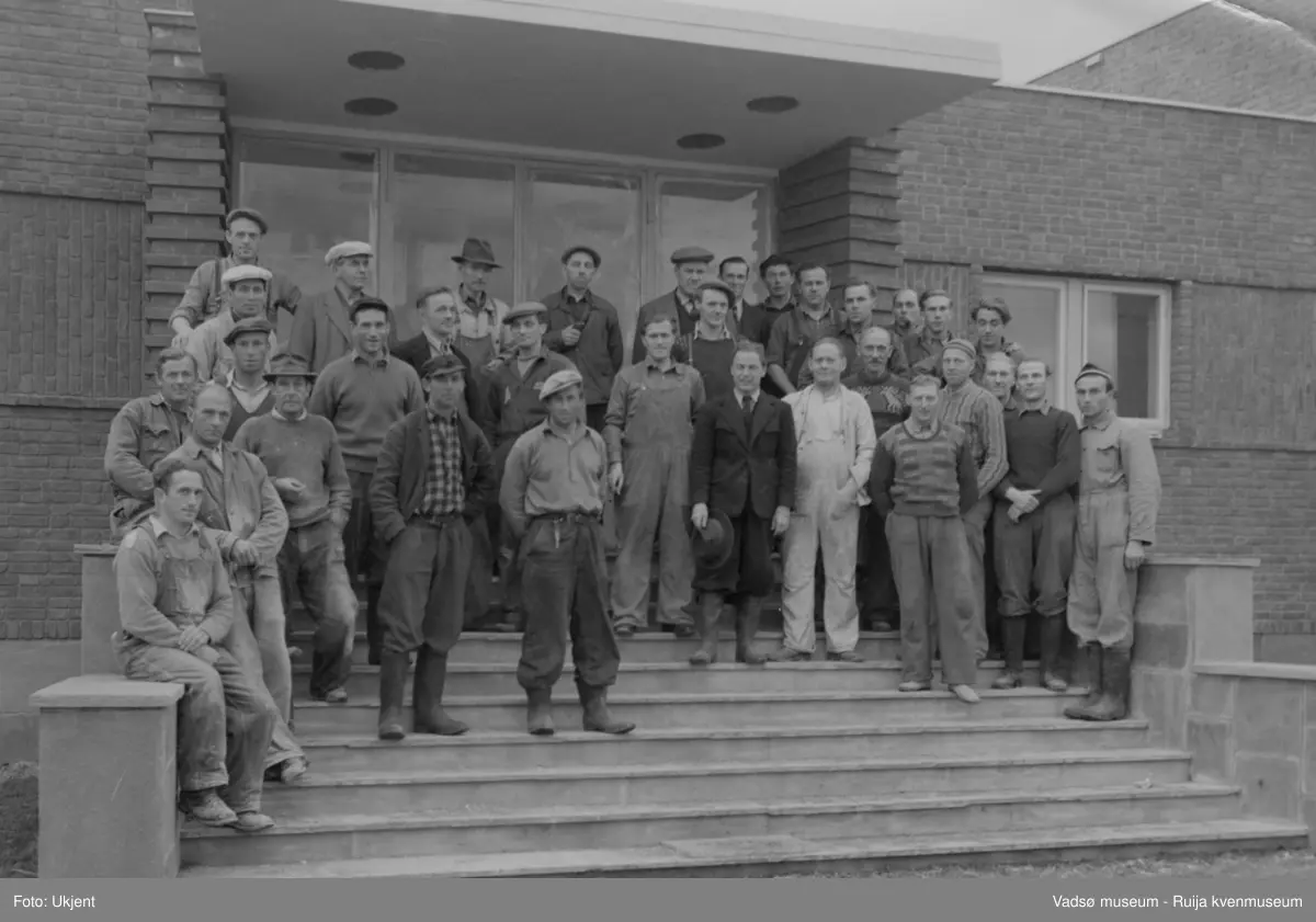 NRK-Bygget i Vadsø. På den store rappa i front av bygningen står en hel gjeng av staute arbeidsfolk som var med å reise det nye NRK-bygget i Vadsø 1948-49. Mennene er kledd i arbeidsklær, bl.a. i overaller, skjorter, kjeledresser og noen med hatt, lue eller sixpence på hodet.
Finnmark kringkaster (NRK-bygget) i Vadsø, byggeår 1949. Arkitekt Henrik L. Kjær. Bygget har bærende betongvegger og fasadene er lagt med teglstein og grunnmuren er belagt med skiferplater. (Kilde: Arkitekturguide for Nord-Norge og Svalbard samt "Fra djevelmaster til Hallo fiskeflåten")