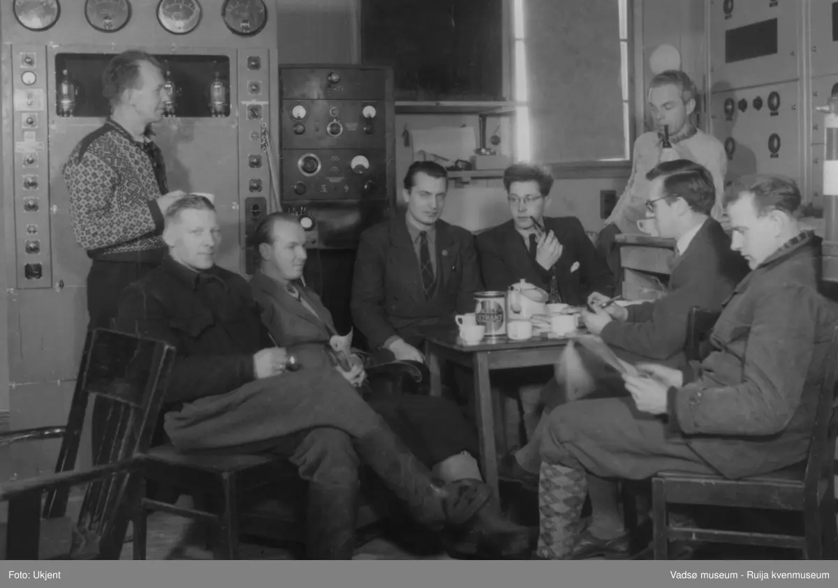 NRK-bygget i Vadsø. Et rom med teknisk utstyr. Rundt et bord sitter og står 8 menn. Bildet er av staben på Finnmark Kringkaster og er tatt våren 1949. På bordet ser vi kaffekjele, kaffeboks, kaffekopper og fløtemugge. Noen av mennene røyker pipe.
Fra venstre ser vi; bestyrer Arne Torp, montør Aage Huru, teknikerne Nils Fr. Jørgensen og Erling Grønvigh, assistent Ivar Balsvik, fungerende programsekretær Ivar Holm, fullmektig Georg Melsvik og montør Harald Zahl. (Kilde:"Fra djevelmaster til Hallo fiskeflåten" Bård Gudmund Hansen)
Finnmark kringkaster (NRK-bygget) i Vadsø, byggeår 1949. Arkitekt Henrik L. Kjær. Bygget har bærende betongvegger og fasadene er lagt med teglstein og grunnmuren er belagt med skiferplater. (Kilde: Arkitekturguide for Nord-Norge og Svalbard)