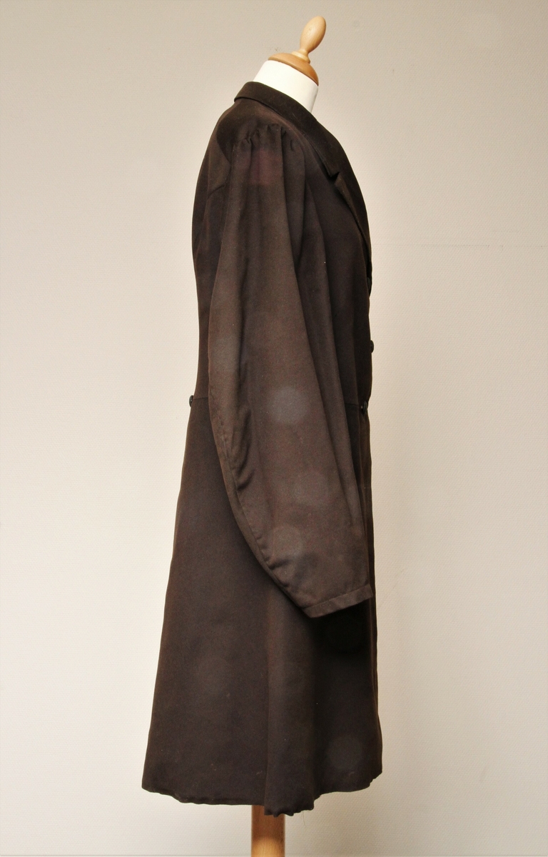 Lang jakke sydd i brunt, blankt ullstoff. Krage med slag, dobbeltspent med trekte knapper. Søm rundt hele livlinja, med unntak av ryggstykkene som er hele. Påsydd to store flak, 55 cm lange. Lang splitt bak, en knapp påsydd bak på hvert flak. En innerlomme, samt to stikklommer i skjørteflakene. Hele jakka er sydd for hånd. Jakka er godt brukt, og det er sydd på lapper i nakken, nederst i ermeforet og i livlinja. 