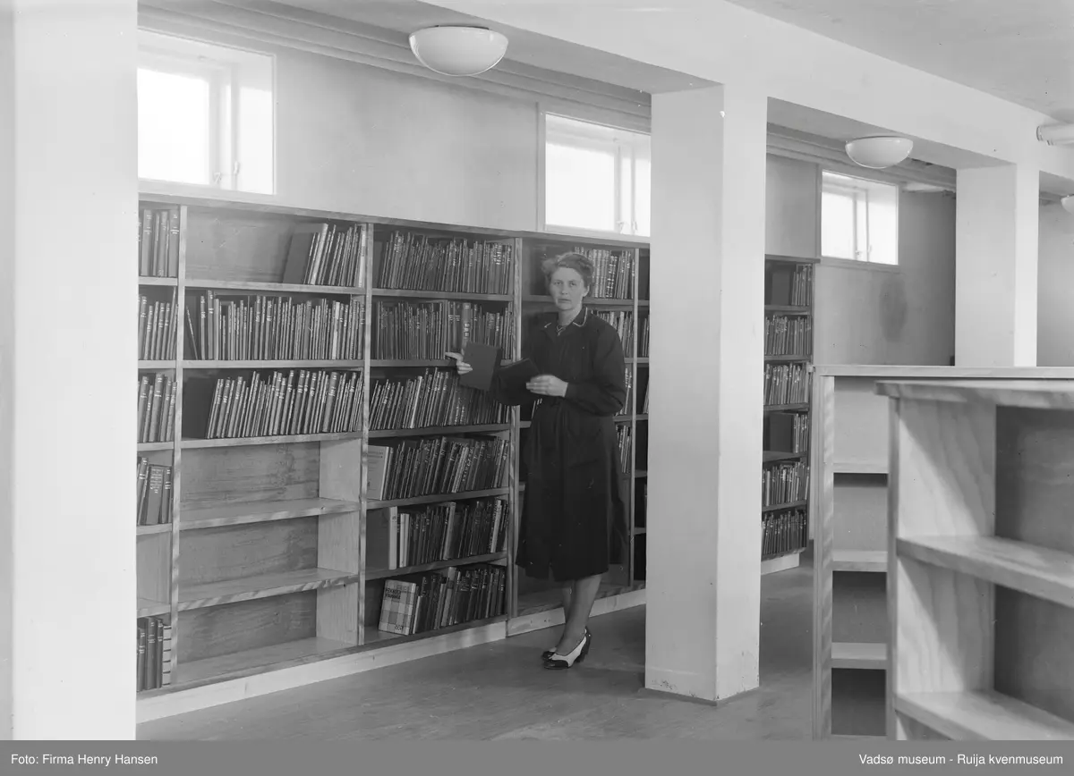 Vadsø rådhus, interiør fra biblioteket som hadde lokaler i sokkeletasjen 1952-1964. Sjefsbibliotekar Birgit Kubberud Frette står ved bokhylla. Rådhuset ble bygd i 1951-1952.