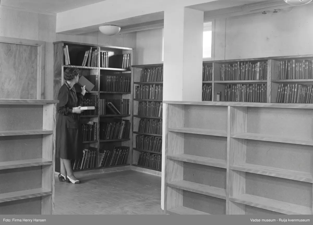 Vadsø rådhus, interiør fra biblioteket som hadde lokaler i sokkeletasjen. Sjefsbibliotekar Birgit Kubberud Frette står ved bokhylla. Rådhuset ble bygd i 1951-1952.