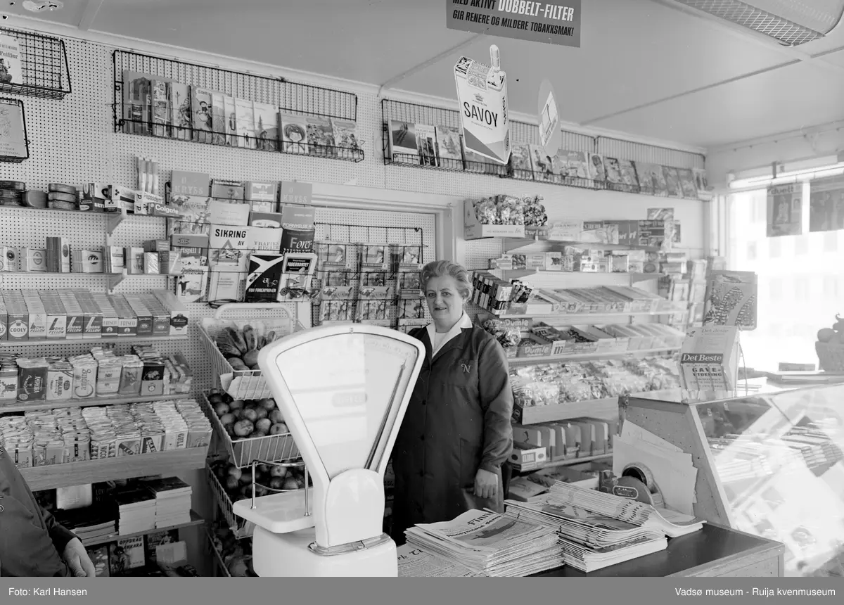 Narvesen kiosk, Vadsø 13.mai 1965. Deler av interiøret og vareutvalget i kiosken. Kioskansatt Anny Iversen.