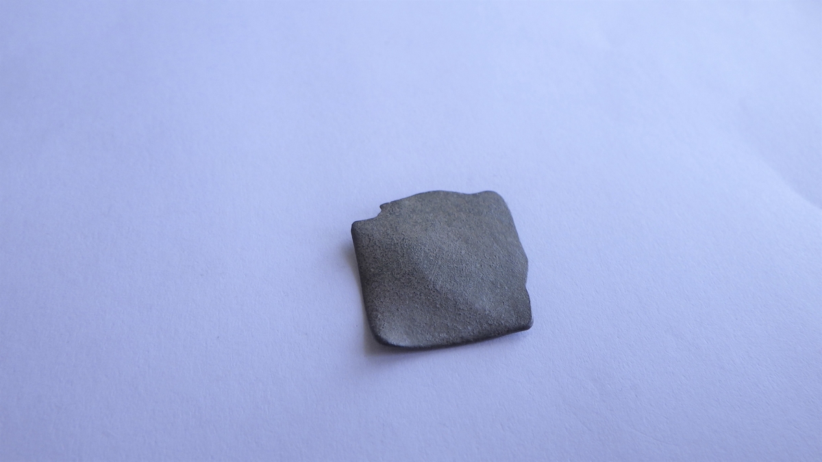 En ujevn metallplate med  kvadratliknende form og to bruddflater. Dette kan være et plateavklipp fra metallhåndverk.