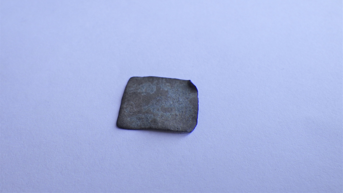 Jevn metallplate med rektangulær form og et innbrettet hjørne. Dette kan være et emne til et platevektlodd.