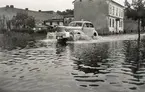 Översvämning på Linnégatan, Växjö, 1940. En bil plöjer fram, bakom den ser man några hus i kvarteret Dalen.