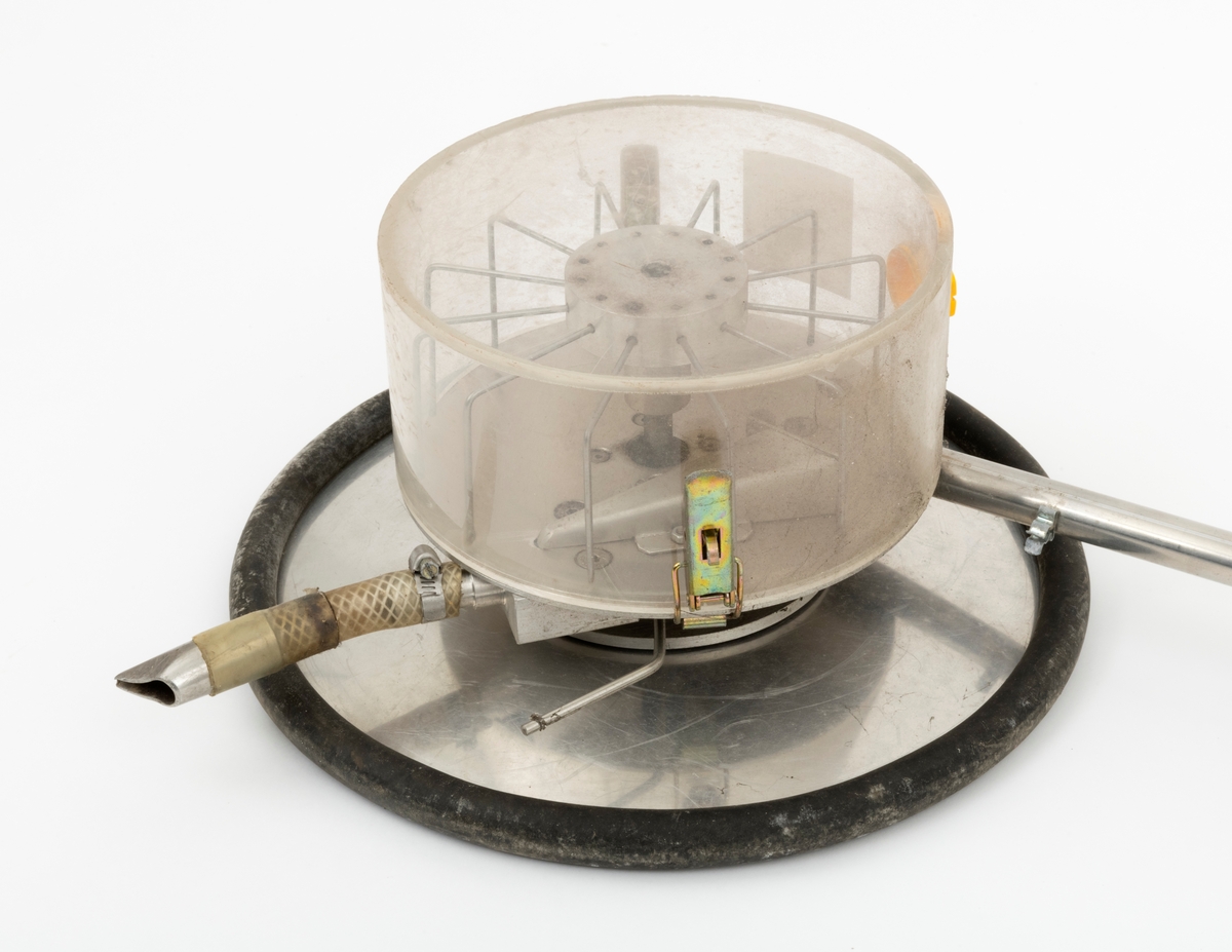 Apparat for stripesåing av skogfrø. Dette later til å være en prototyp fra eksperimentalverkstedet ved NISK (Norsk institutt for skogforskning) på Ås i Akershus. Apparatet er bygd på ei krykke av lettmetall med handtak og underamstøtte av grå plast. Umiddelbart under handtaket er det en lett strambar skrue som holder på plass ei halvmeterlang aluminiumsstang med en kvit gummiholk i ytterenden, et element som antakelig skulle brukes til å styre med i ulendt terreng. I den nedre enden av krykka er det påmontert en sylindrisk frøbeholder av klar plast. Denne beholderen har en diameter på 20 centimeter og en høyde på snaut 10 centimeter. Beholderen kan løsnes ved hjelp av to spenner som er montert på hver sin side av sylinderen. Inne beholderen ser vi en skags visp med ståltrådtinner. Denne roterer med et hjul, lagd av ei lettmetallplate om med svart gummiforing lags ytterkantene. Diameteren på dette hjulet er drøyt 32 centimeter. Påfylling av frø må ha skjedd via en åpning i plastsylinderen som ellers er stengt ved hjelp av en gul plastmutter. Frøet faller mot marka via en kort slangestubb som er utstyrt med metallmunnstykke.