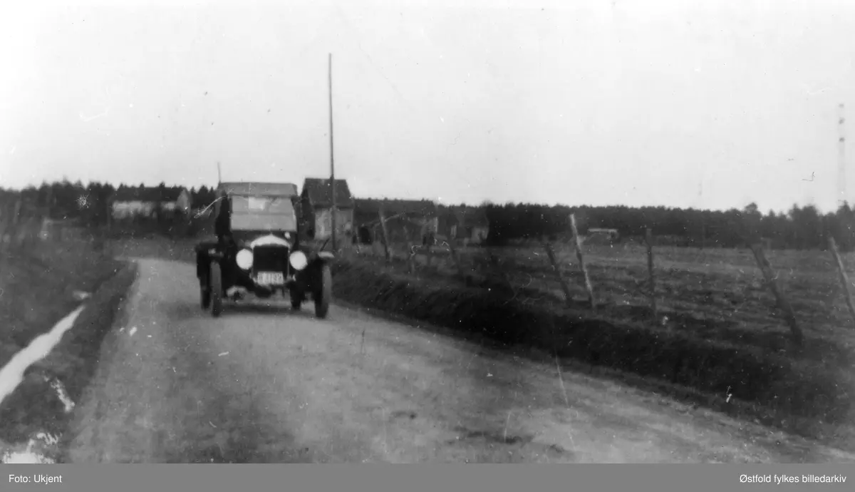 Ford personbil, trolig årsmodell 1925-27. Bilen tilhørte Kristian Sulusnes fra Varteig. Den ble brukt til fiskebil, Sulusnes kjørte rundt på gårdene og solgte fisk i Varteig. Gården i bakgrunnen er Hasle, tilhørte Finn Mathisen.