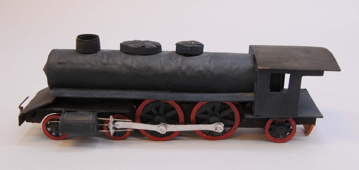 Leksaksånglok (:7) med tender (:8) av huvudmaterialet papp. Delarna är limmade eller sammanfogade med rött lack. Loket har fem hjulpar. Två av dem är av större diameter och kopplade via silvermålade koppelstänger. Hjulen är gjorda av papp och hjulaxlarna av runda träpinnar. Loket är målat i svart och hjulringarna i rött.
I lokets främre ände och i tenderns (:7) bakre ände finns koppel av ståltråd. Loket och tendern har varit sammanfogade med ett snöre men lacket som höll det på plats har lossnat från tendern och hänger från ångloket.