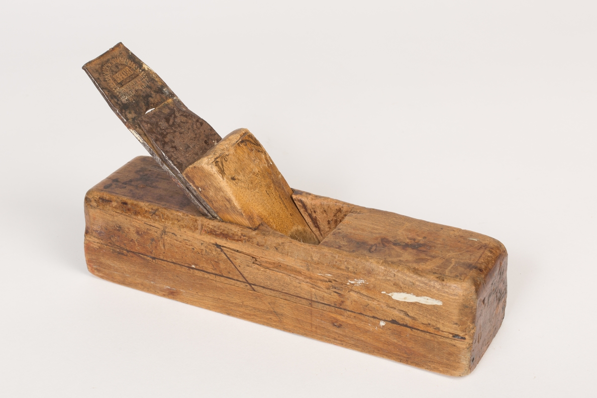 Høvel med tilnærmet kvadratisk tverrsnitt og plan såle. Har høveljern, klaff og kile. Stokkens oversider har utsparinger. Kilen er dekorert med et liljemønster (blyanat?) og har tynne dekorlinjer langs stokkens overflate og en midt på hver sideflate. Sporene etter slag på stokkens bakre kortside - i forbindelse med at høveltangen (jernet) skulle stilles/reguleres. 
Spor etter råte i et mindre felt på høyre langside.
Sålen er av bøk og øverste del av stokken er i bjørk.