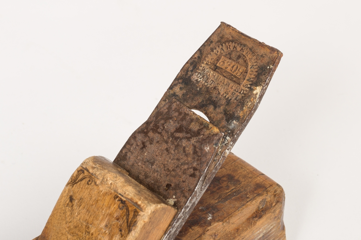 Høvel med tilnærmet kvadratisk tverrsnitt og plan såle. Har høveljern, klaff og kile. Stokkens oversider har utsparinger. Kilen er dekorert med et liljemønster (blyanat?) og har tynne dekorlinjer langs stokkens overflate og en midt på hver sideflate. Sporene etter slag på stokkens bakre kortside - i forbindelse med at høveltangen (jernet) skulle stilles/reguleres. 
Spor etter råte i et mindre felt på høyre langside.
Sålen er av bøk og øverste del av stokken er i bjørk.