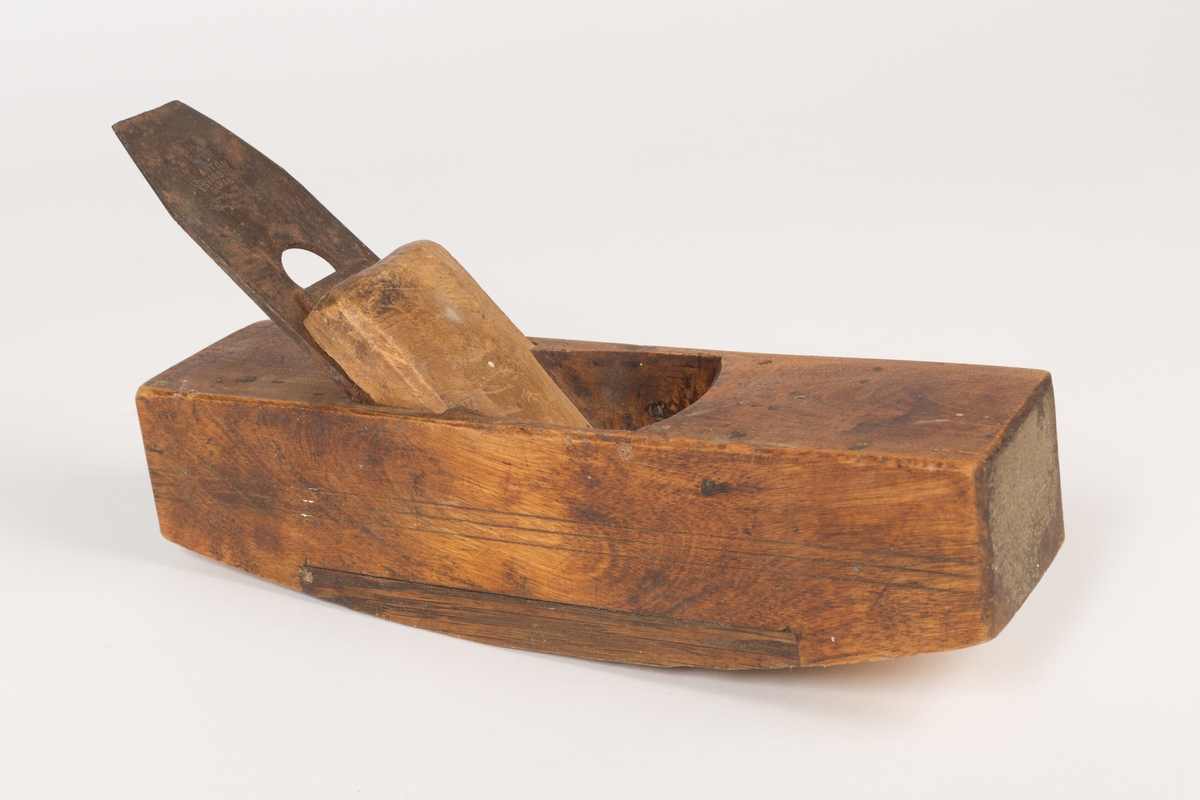 Buehøvel med høvelstål, klaff (sponbryter) og kile. Høvelstokken har buet såle og tre paralelle dekorstreker risset inn langs begge sidene. Et lengre felt av sålen er innfelt med et stykke hardere treverk (eik/nøttetre?). Oljet.