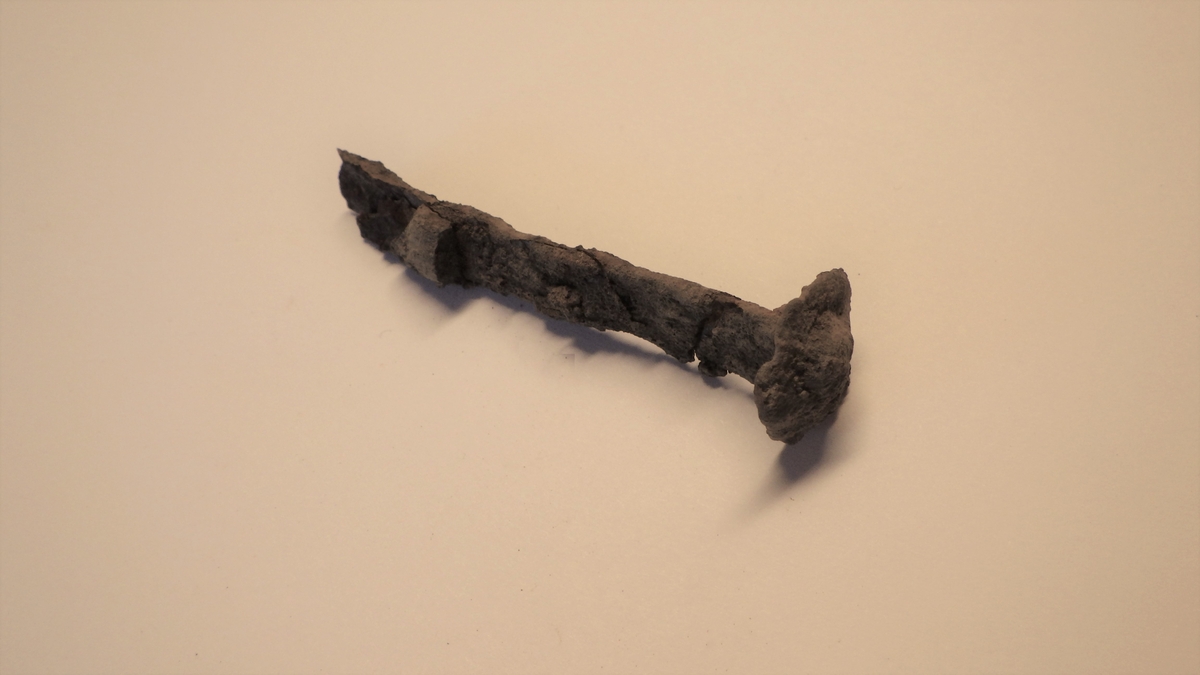 MALV: L. 6, 2 CM, AVLANGT, FLATT JERN M. REKTANGULÆRT TVERRSNITT. TIL-NÆRMET SIRKULÆRT HODE. I MOTSATT ENDE AV HODET ER DET FESTET ET FLATTJERNSTYKKE PÅ HVER SIDE. 