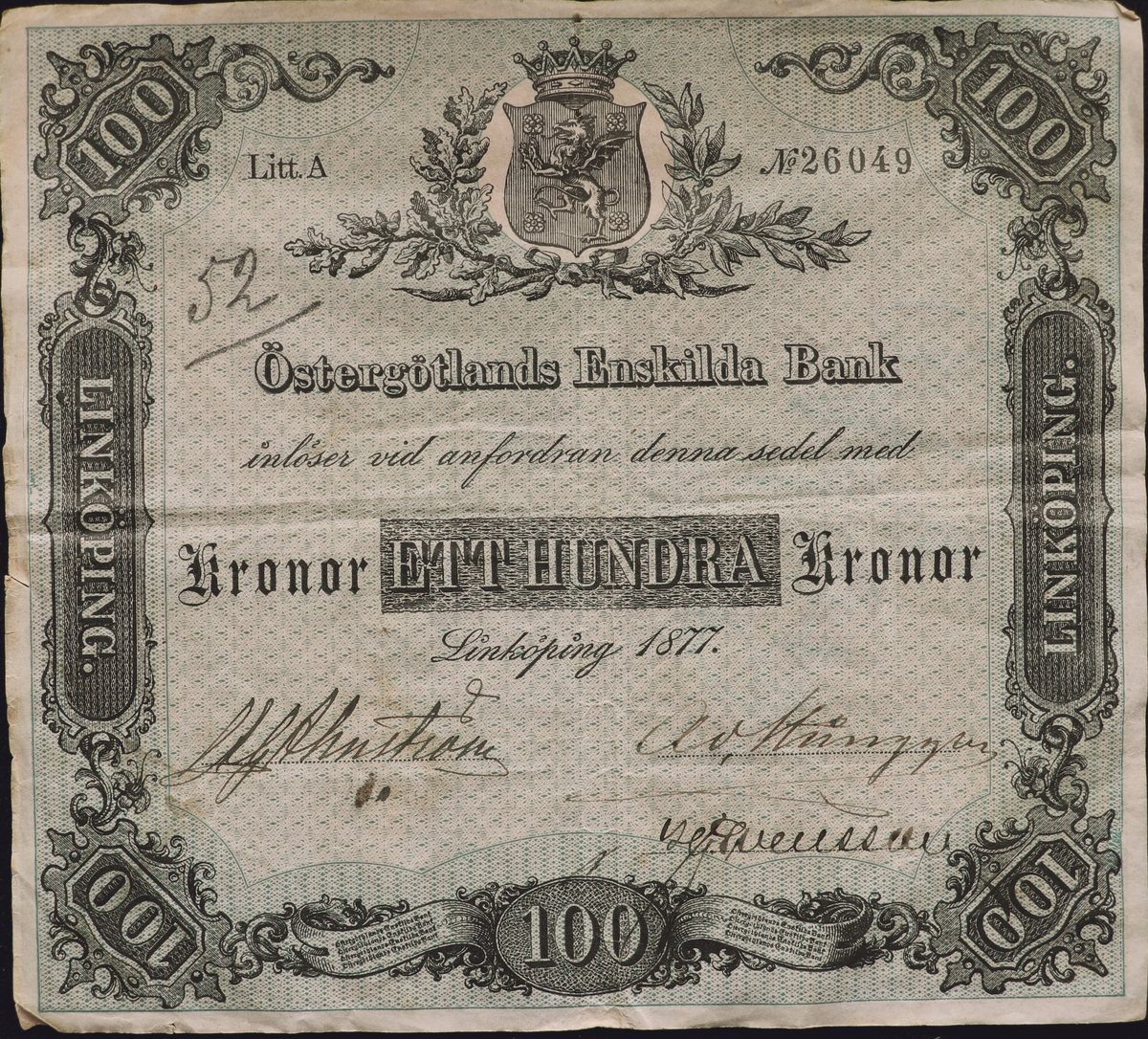 En grön sedel på hundra kronor från Östergötlands Enskilda Bank från1877. Serienummer 26049, skrivet till höger på sedeln. Tre signaturer på sedeln. Högst upp i mitten finns Östergötlands landskapsvapen. 
Baksidan har samma tryck som framsidan men spegelvänt och pappret är rött. I mitten är också ett emblem där det står Östergötlands Enskilda Bank.
Sedeln är fastklistrad på en pappbit. 52 är skrivet med blyerts på vänster sida.