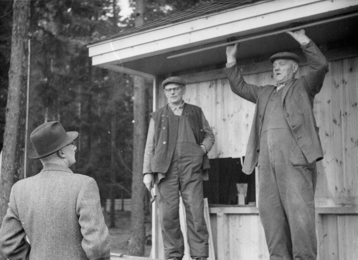 Folkets Park i Linköping. Tre män står vid en liten träbyggnad. En håller en hammare i handen. 1940-tal.
