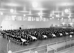 Foto i en stor sal där människor sitter runt långbord.