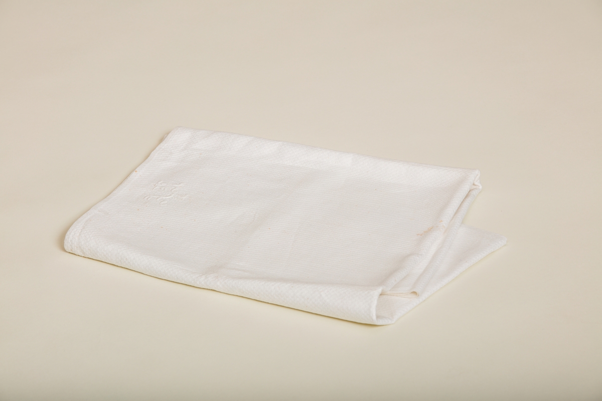Håndkle av hvit lin med mønstereffekt i vevningen. Maskinsydd fold i hver ende. Hvitt håndbrodert monogram i plattsøm. Påsydd hank av bomullsbånd.