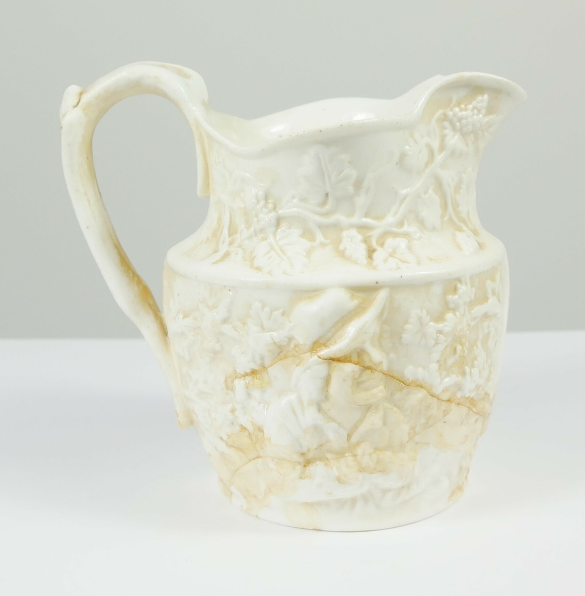 Greiner med blader rundt den øverste delen av muggen. En mann med hatt omgitt av blader på den ene siden på muggen, på den andre siden et motiv med to personer med vinglass