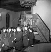Scouter uppställda på led framför en scoutledare. De befinner sig i kyrkan.