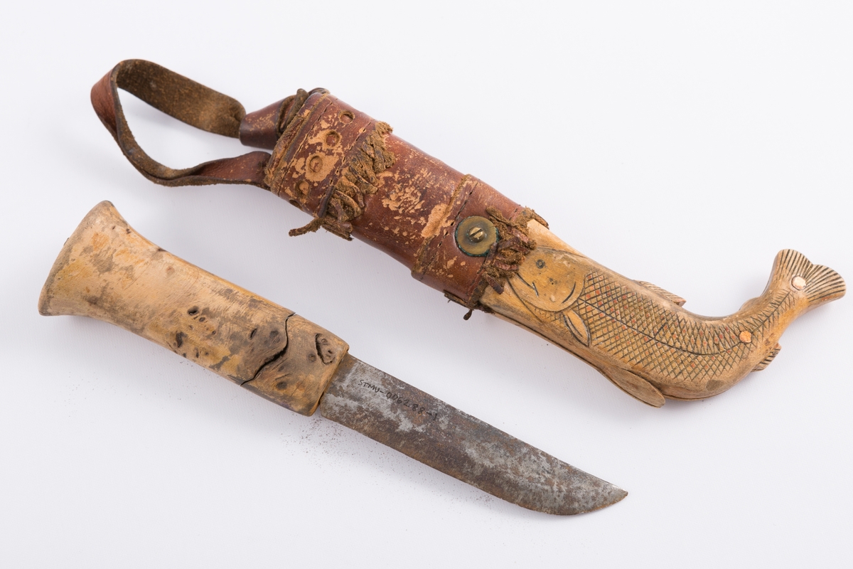 Tollekniv med slire og beltehempe i lær. Skaft tilvirket av lakkert treverk mens slire av lær og treverk. Nederste delen av sliren formet som en fisk.